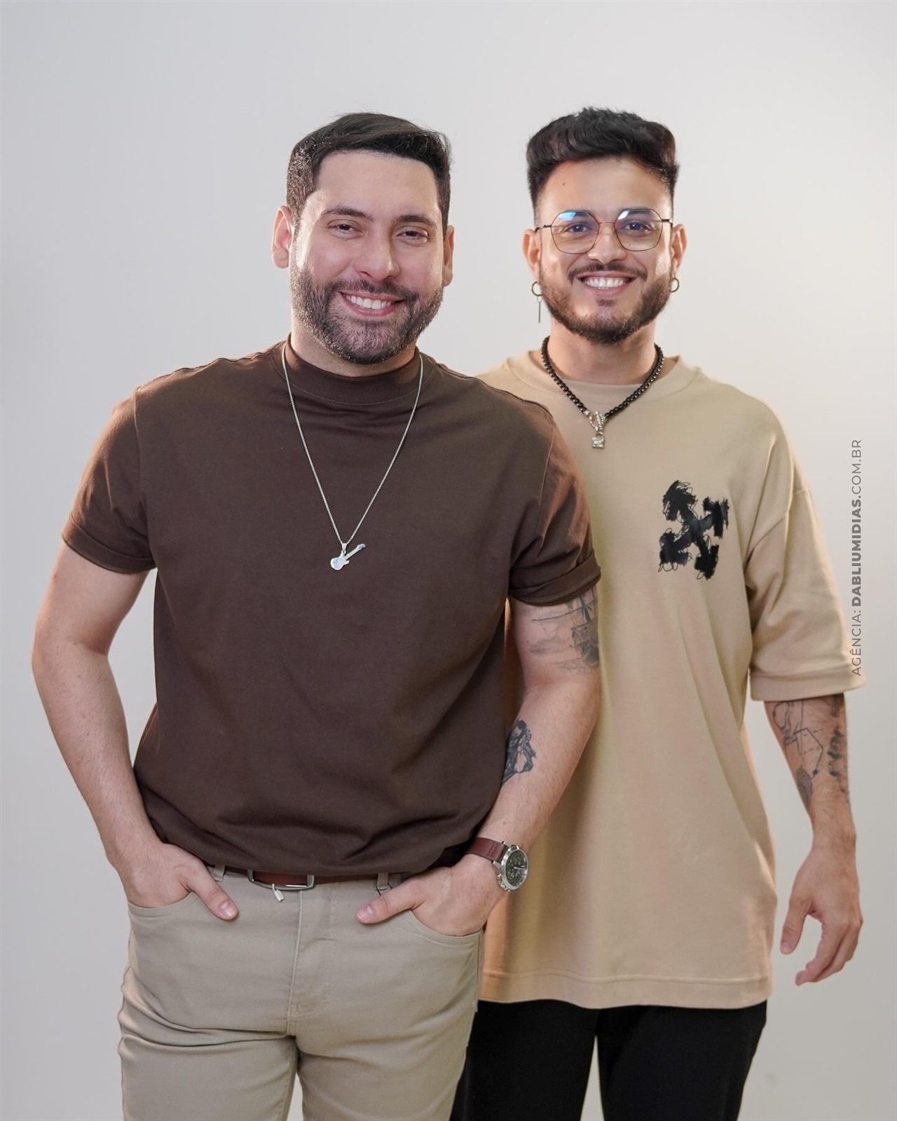 Ensaio fotográfico da dupla George e Kevyn sorrindo em fundo claro de estúdio