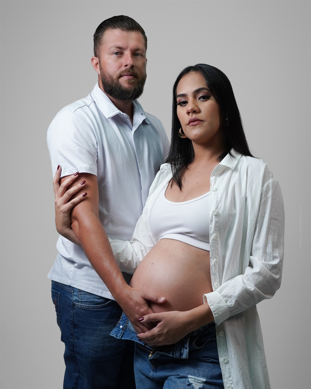Ensaio fotográfico de gestante com o casal Luiz e Pamela vestindo branco e jeans no estúdio em Ariquemes