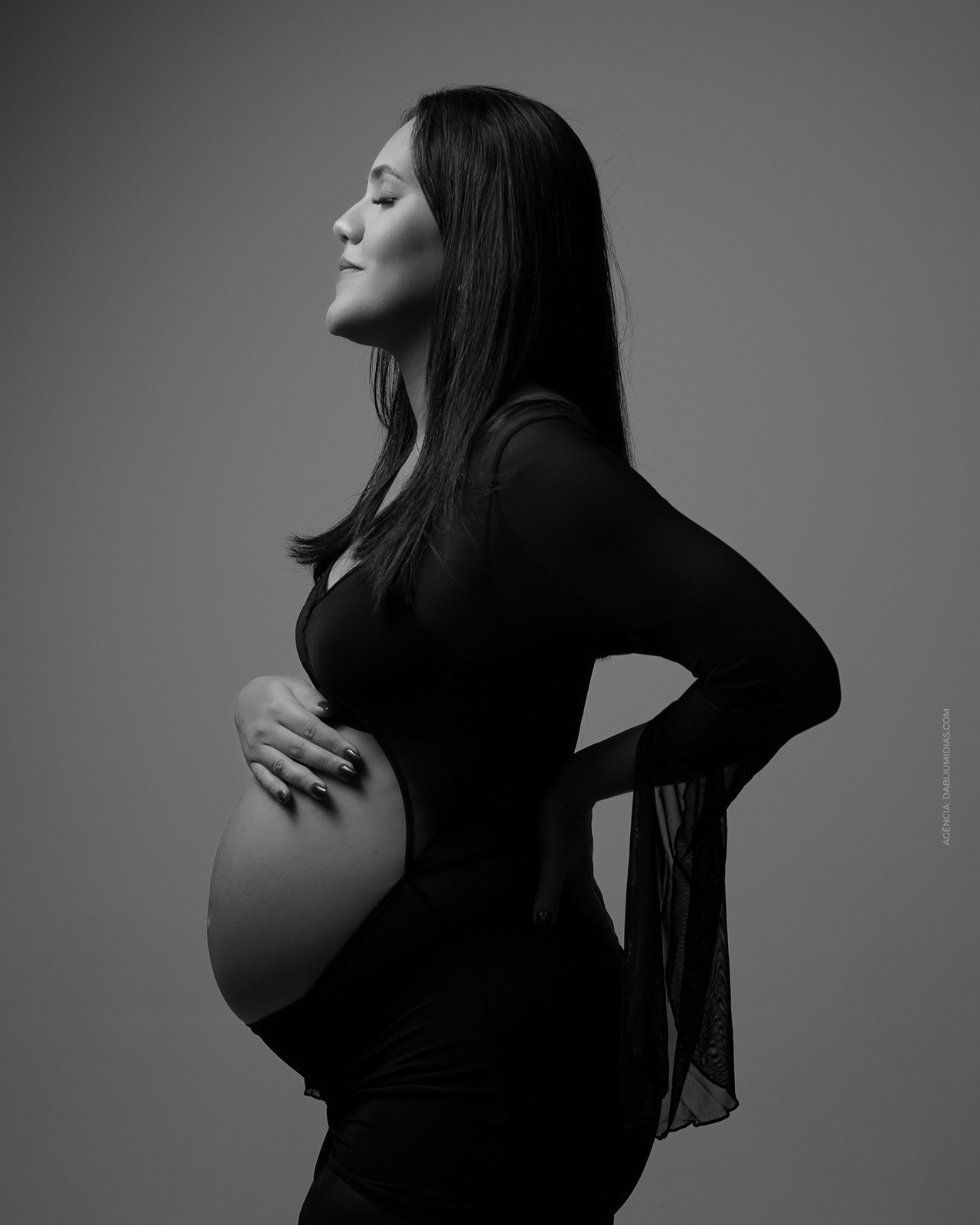 Ensaio de gestante em estúdio em Ariquemes, foto em preto e branco de perfil com a mão na barriga